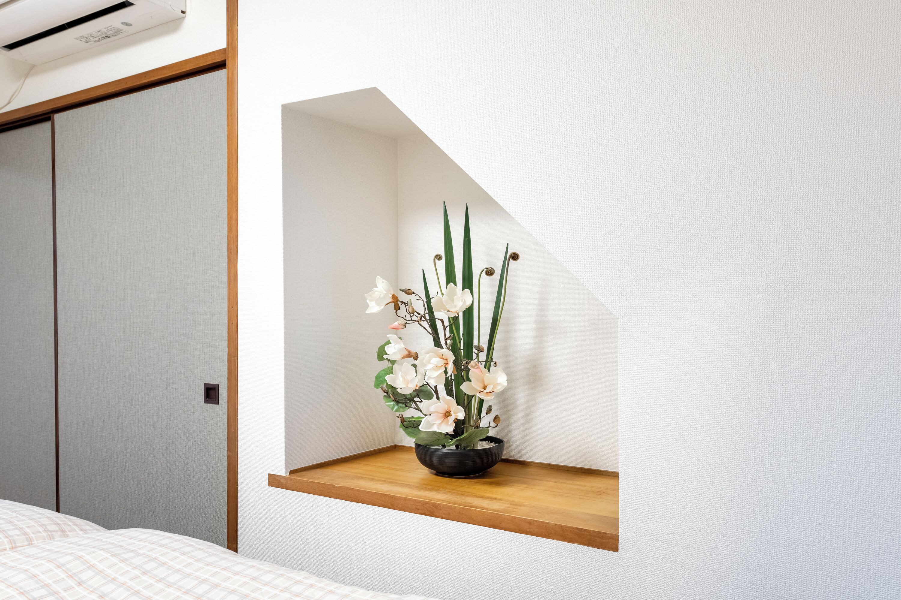 Quarto com cama, prateleira fixada na parede com planta em vaso e porta de correr.