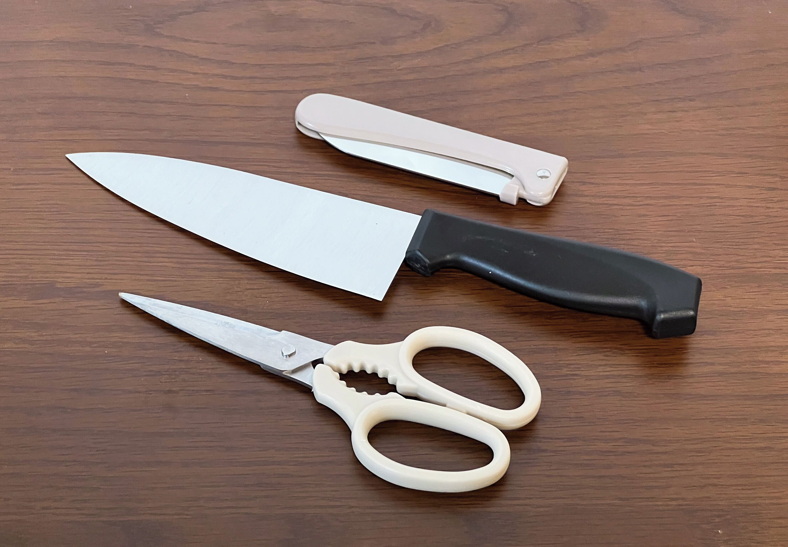 A pair of scissors and a knife with a black handle on a wooden surface.