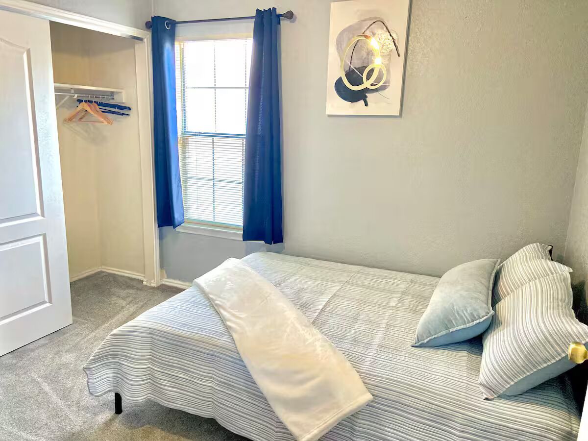 Quarto com cama, guarda-roupa, janela com cortinas e luminária fixada na parede.
