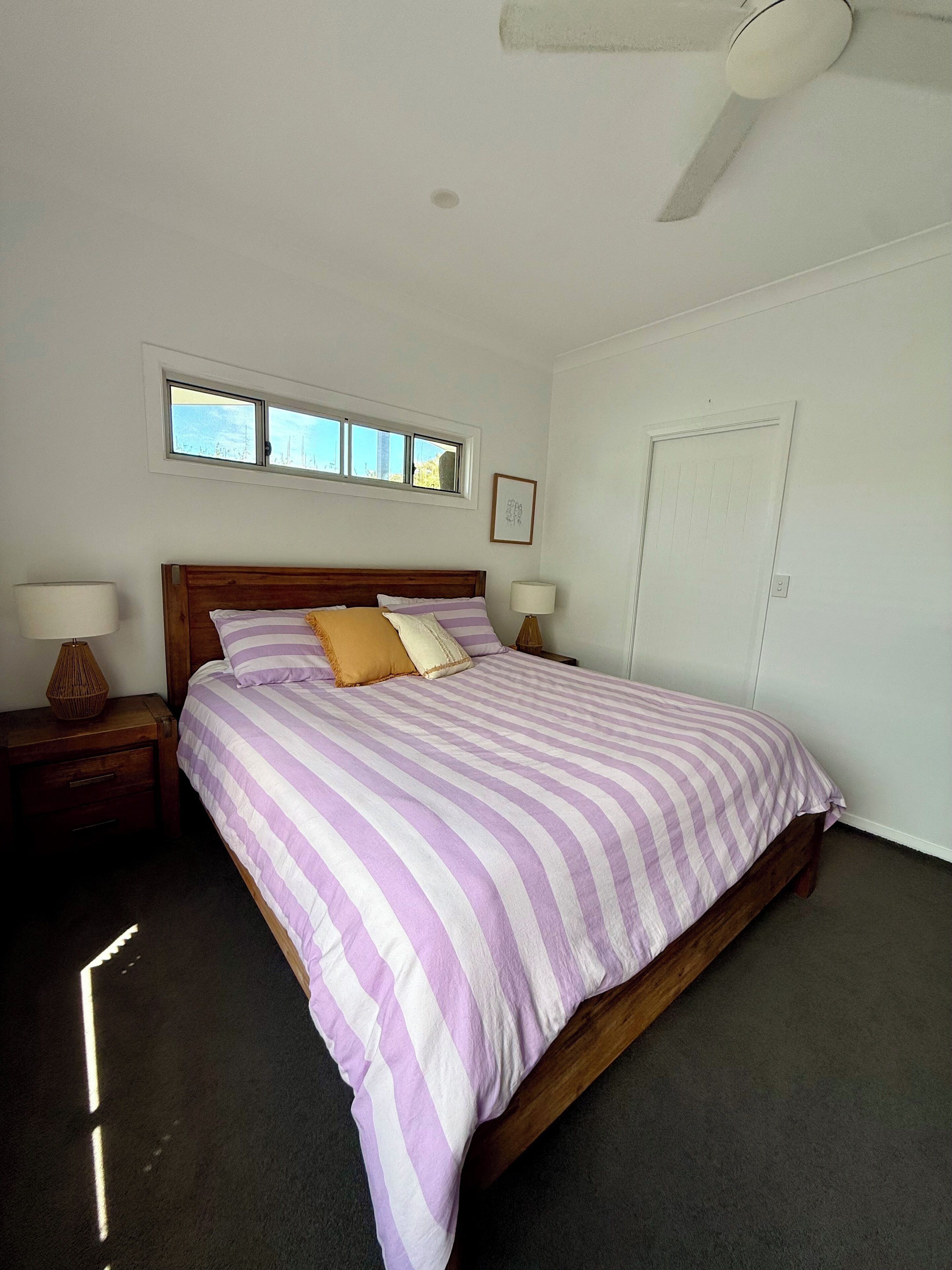 A bedroom with a bed, two bedside tables, a window, a door, and a ceiling fan.
