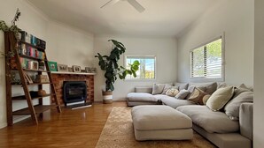 Una sala de estar con un sofá modular, una chimenea, una estantería de madera en escalera y una planta grande.