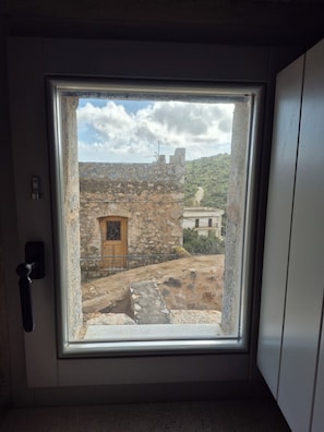Une pièce dotée d’une fenêtre donnant sur une cour intérieure, avec des bâtiments en pierre et une porte en bois.