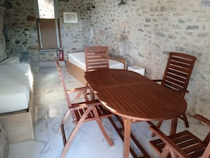 Une pièce avec un mur en pierre, un lit, une table en bois avec des chaises et un petit meuble blanc.