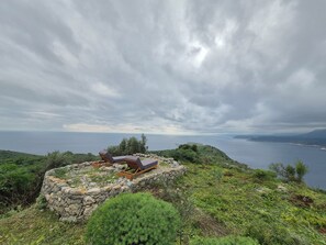 A stone structure with two lounge chairs overlooking a body of water and distant land. - Torre Agetria Blacherna: Live the fullest of the Mani experience (Stavri)