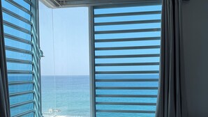 Quarto com cama, mesa de cabeceira e vista para o mar através de grandes janelas.
