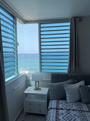 Un dormitorio con cama, mesita de noche y vistas al mar a través de amplios ventanales.
