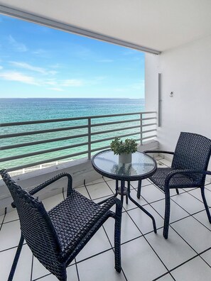 A balcony with a glass table, two wicker chairs, and a potted plant. - Oceanfront Condo • Balcony • Pool & Beach Access (Rincón)