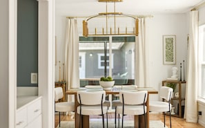 Un coin repas avec une table en bois, des chaises blanches et un lustre.