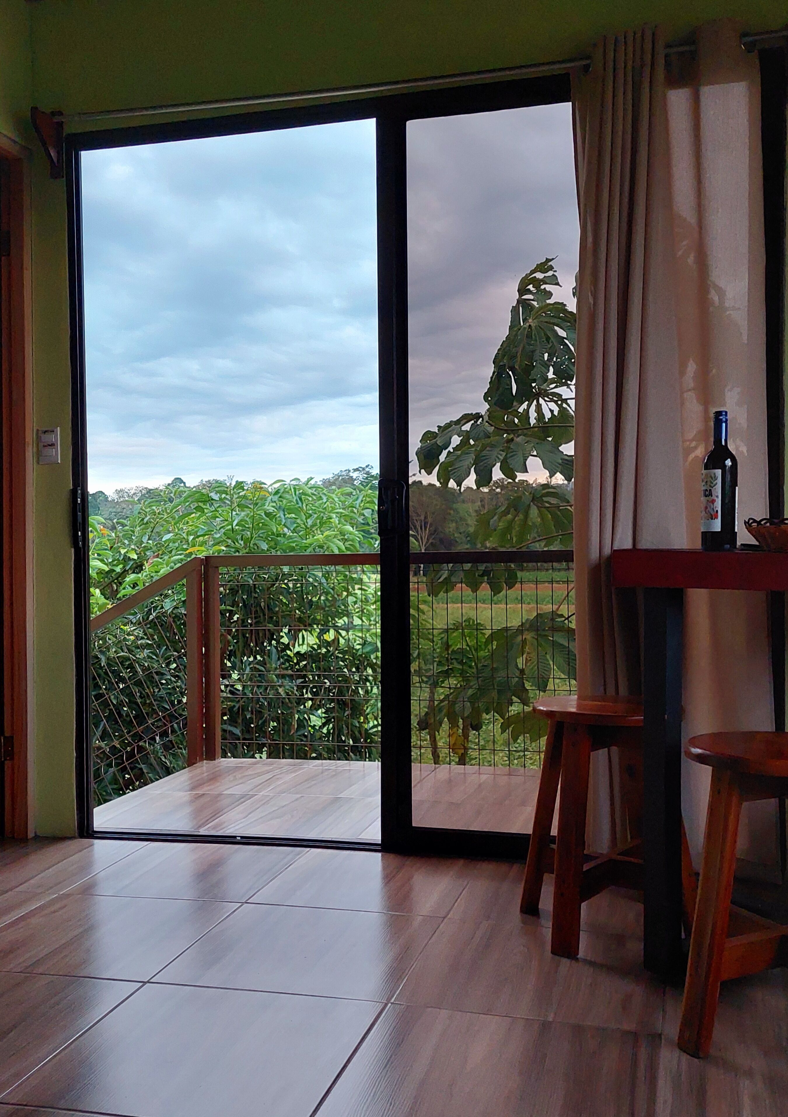A room with a large sliding glass door leading to a balcony with a view of a garden and trees.