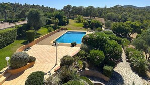 Una piscina circondata da giardini curati, un vialetto lastricato e una vista su un paesaggio collinare.