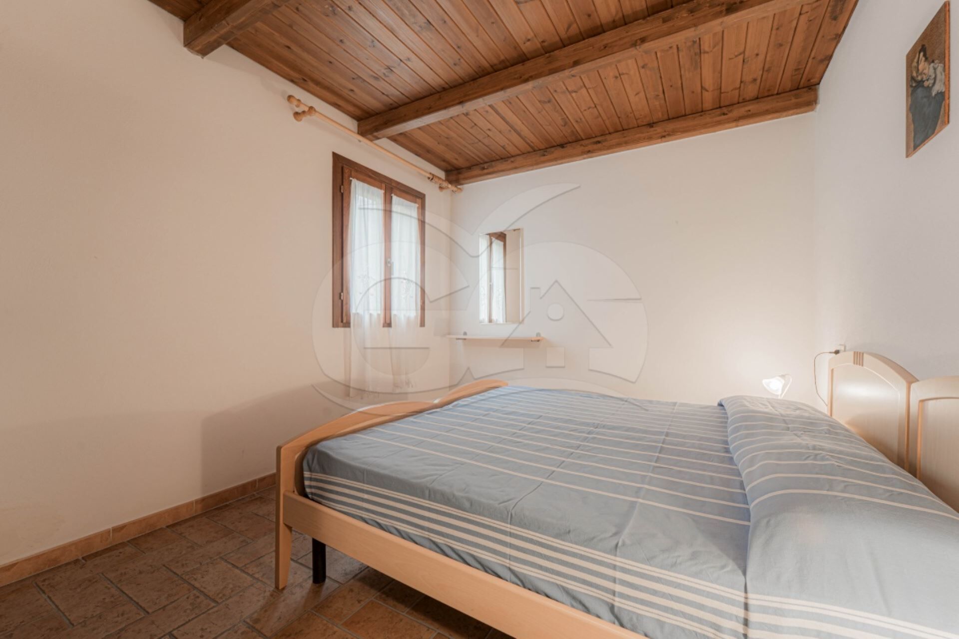A bedroom with a wooden ceiling, a bed with a striped bedspread, a window, and a small desk.