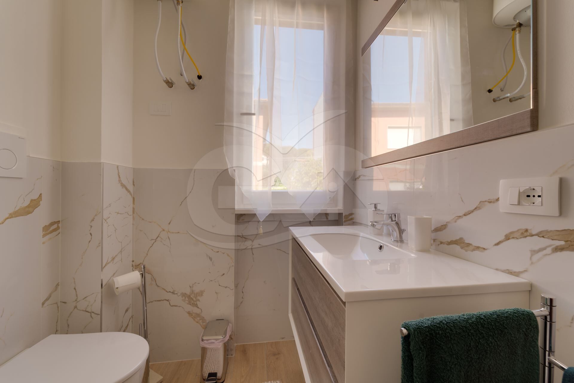 Een moderne badkamer met een marmeren wand, een witte wastafel, een spiegel en een handdoekrek.