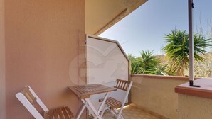 Un balcon avec une table en bois et deux chaises, un sol carrelé et une vue sur des palmiers.