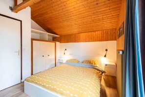 A bedroom with a wooden ceiling, a bed with patterned bedding, bedside lamps, and a wardrobe. - Apartment Balcon du Léman (Thollon-les-Mémises)