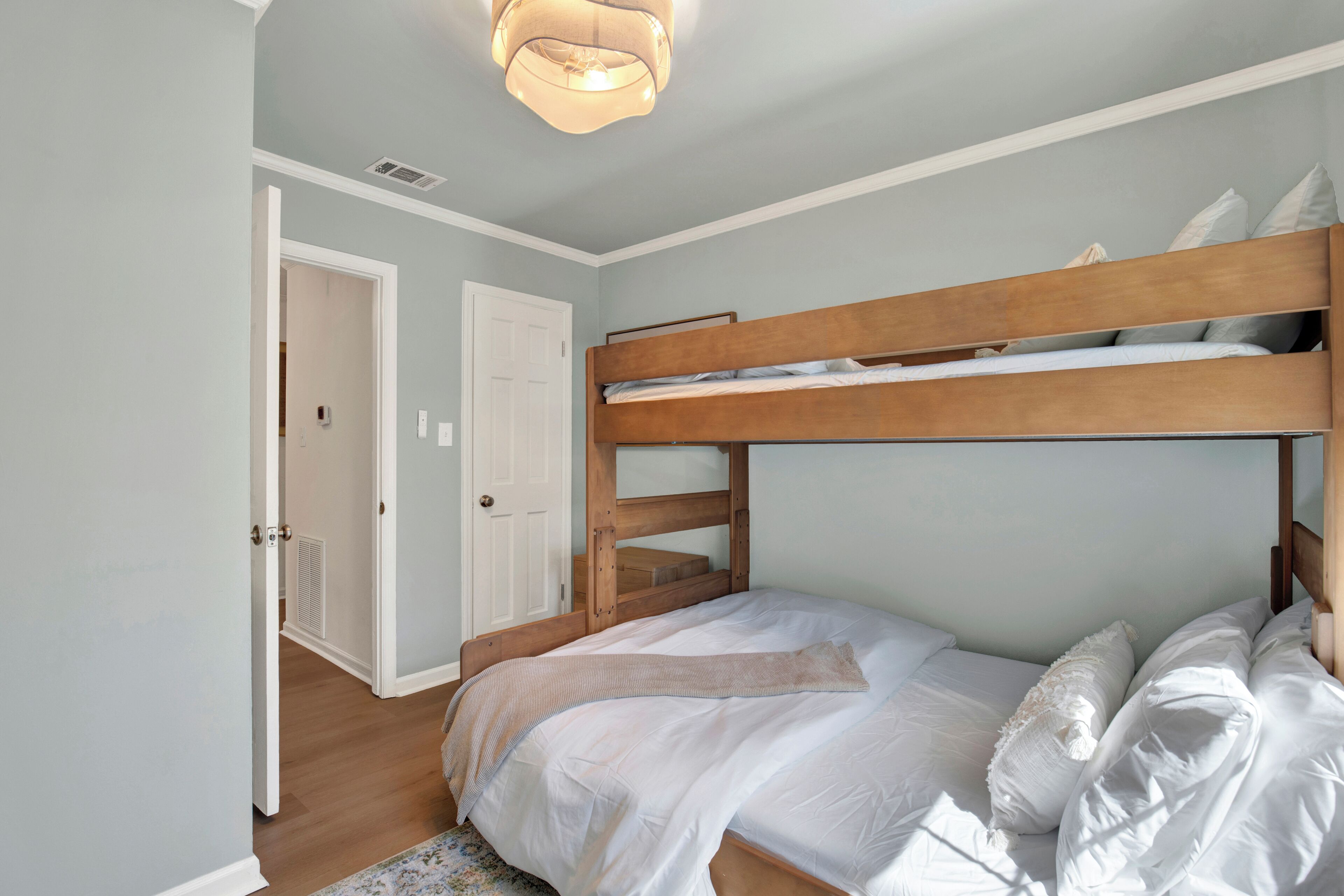 Un letto a castello con struttura in legno, biancheria bianca e un tappeto chiaro sul pavimento.