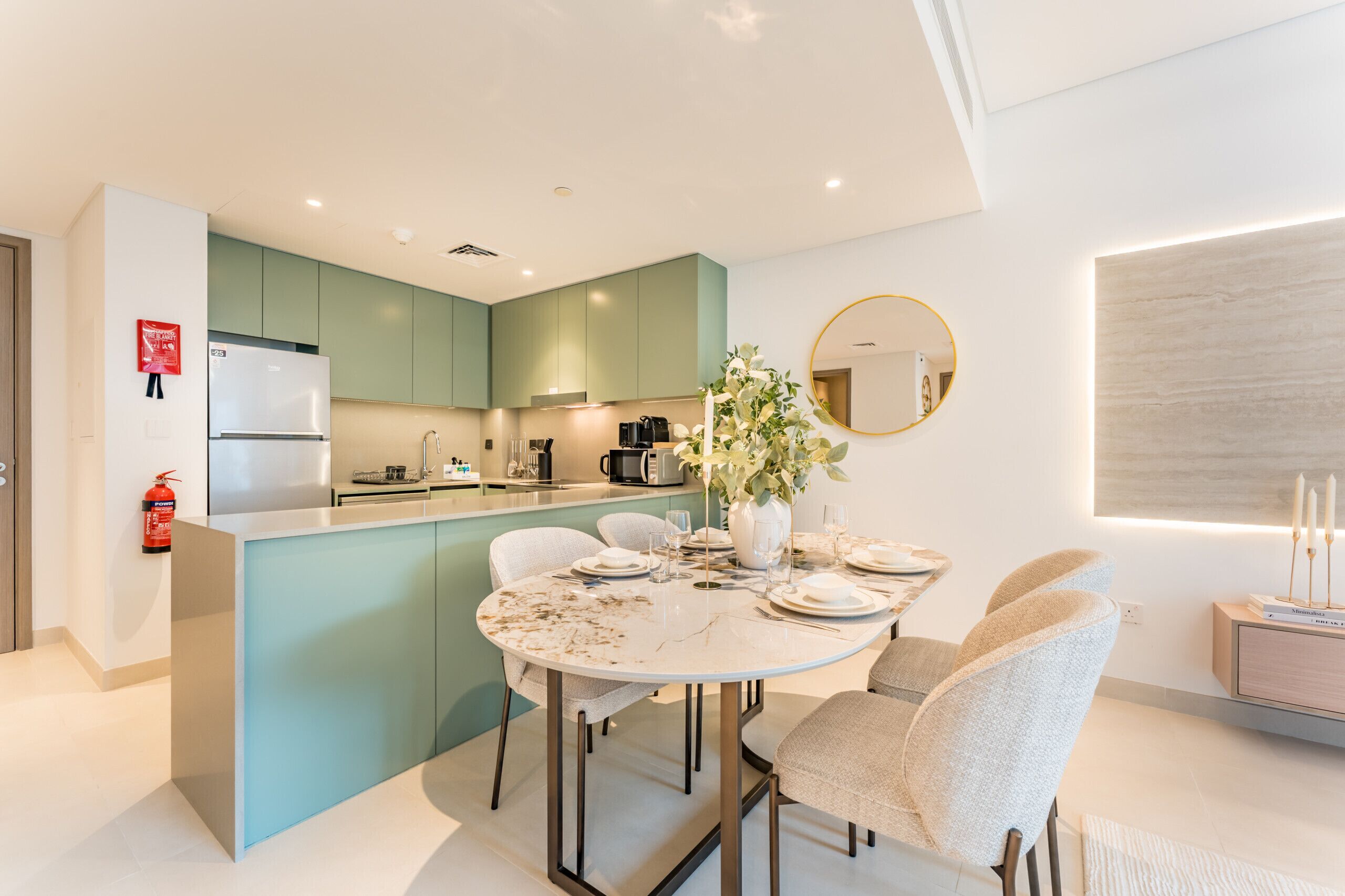 A modern kitchen with teal cabinets, a white island, and a dining area with a round table and chairs.