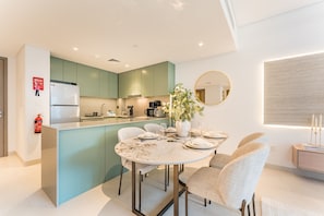 A modern kitchen with teal cabinets, a white island, and a dining area with a round table and chairs. - Rustic 1BR Apartment, Perfect Walk to Central Park - Myrtle, Al Wasl (Dubai)