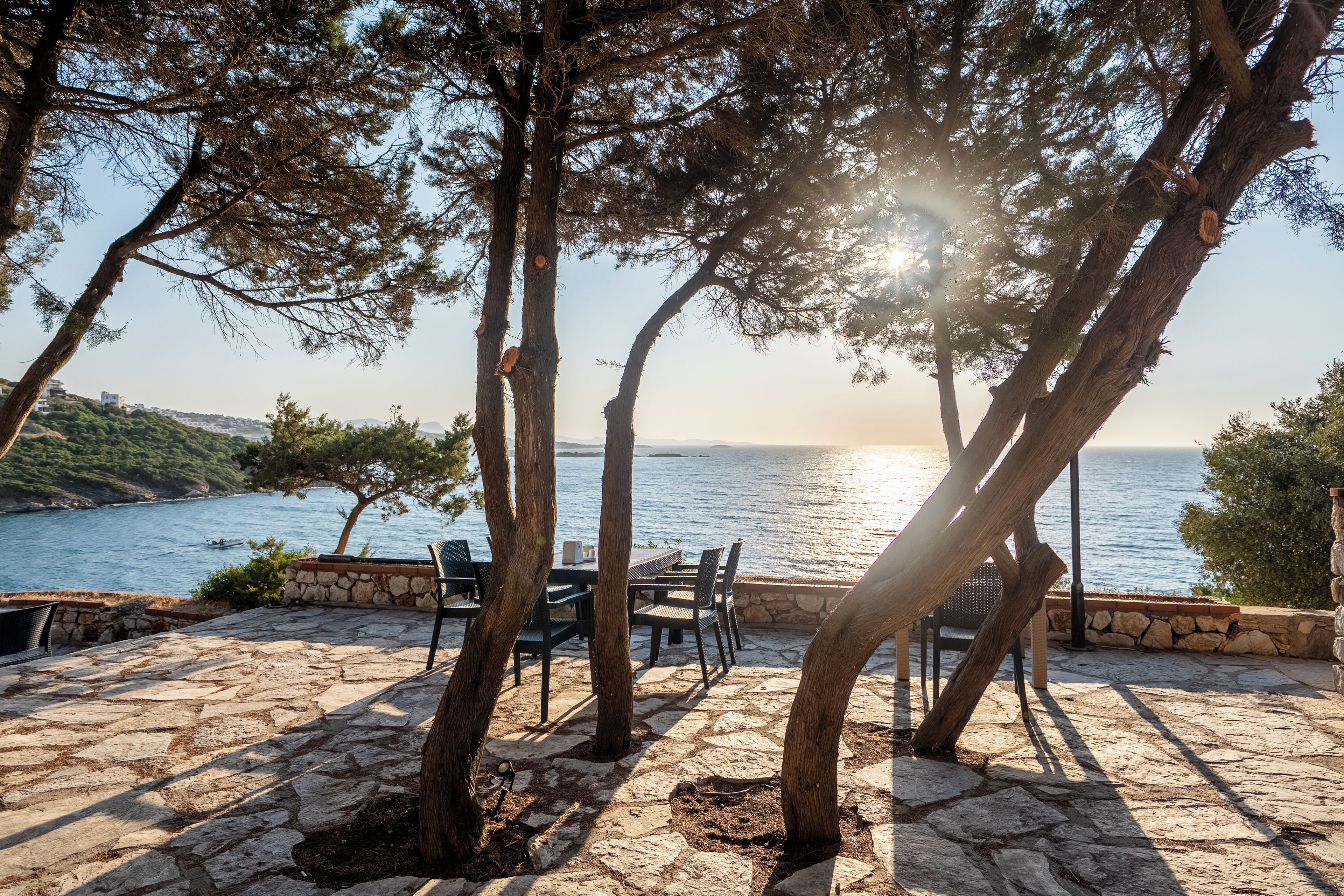 A stone patio with outdoor furniture overlooking a body of water.