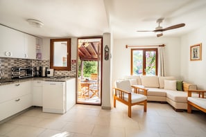 A compact kitchen with a dishwasher, a dining area with a table and chairs, and a living area with a sofa and a ceiling fan. -  Denize sıfır Villa•Özel Plaj•Doğal Havuz•Bodrum (Mugla)