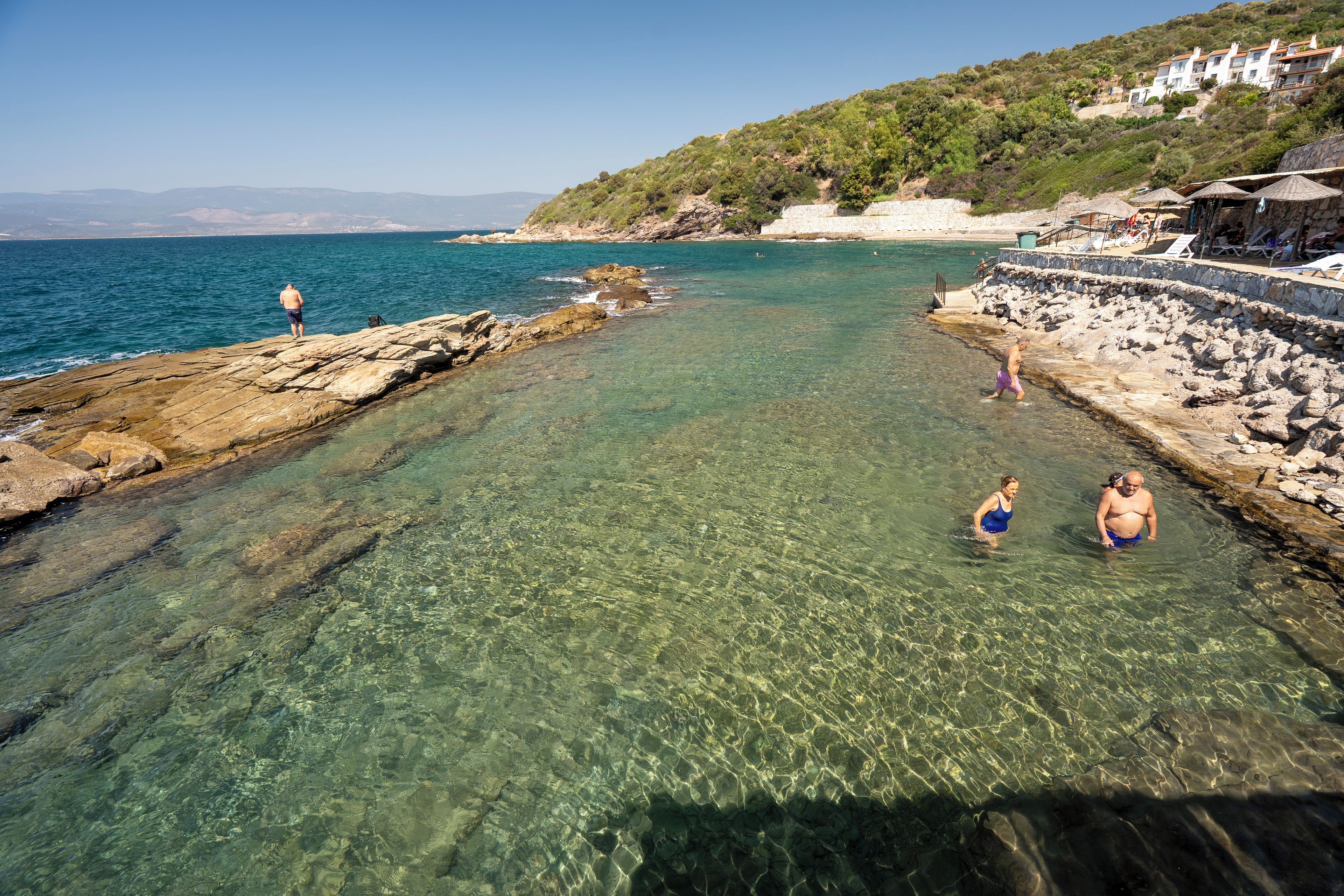 A coastal area with clear water, rocky shorelines, and buildings on a hillside.