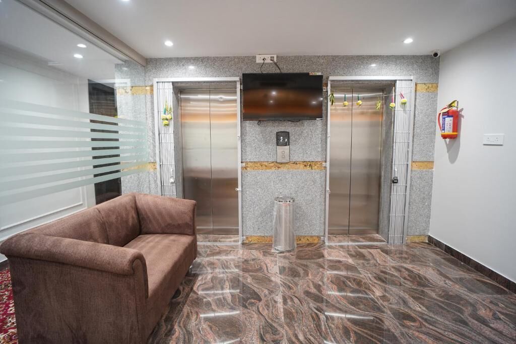 A lobby with a marble floor, a brown sofa, two elevators, a fire extinguisher, and a television mounted on the wall.