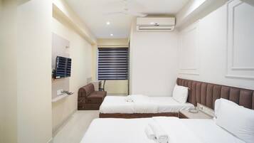 Habitación de hotel con dos camas, un sofá, un ventilador de techo, un equipo de aire acondicionado y una ventana con persianas.