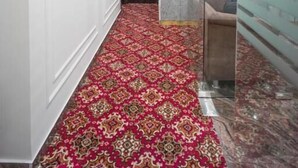 A hallway with a patterned carpet, a glass wall, and a door leading to another room. - Hotel SG International  (Kolkata)