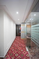 A hallway with a patterned carpet, a glass wall, and a door leading to another room.
