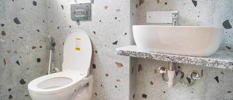 Un baño con inodoro y lavamanos blancos, y piso de terrazo.