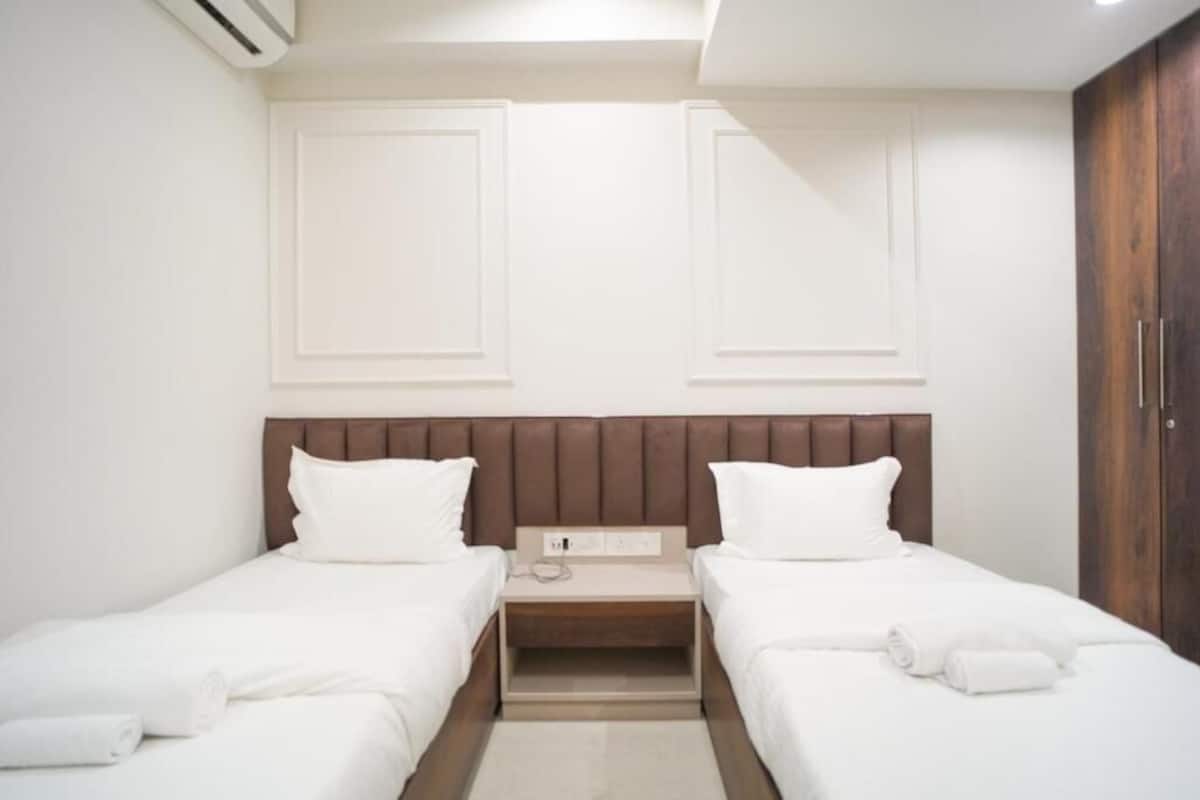 A hotel room with two single beds, a wooden headboard, a small bedside table with a phone, and a wardrobe.