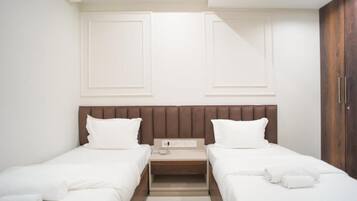 Una habitación de hotel con dos camas individuales, cabecero de madera, una mesita de noche con teléfono y un armario.