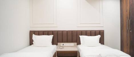 A hotel room with two single beds, a wooden headboard, a small bedside table with a phone, and a wardrobe.