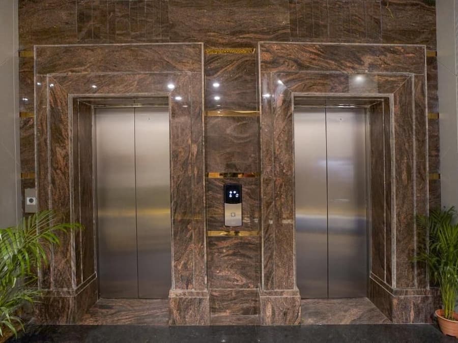 A pair of elevators with marble walls and a digital control panel in the center.