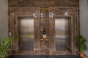 A pair of elevators with marble walls and a digital control panel in the center.