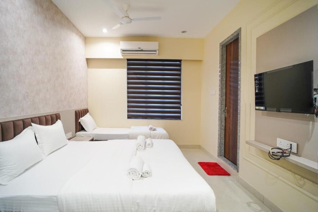 A hotel room with two beds, a TV, an air conditioner, and a window with blinds.