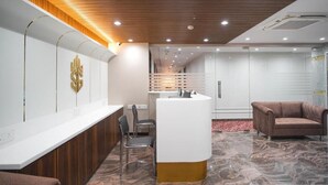 A reception area with a wooden ceiling, a reception desk, a brown leather sofa, and a patterned floor. - Hotel SG International  (Kolkata)