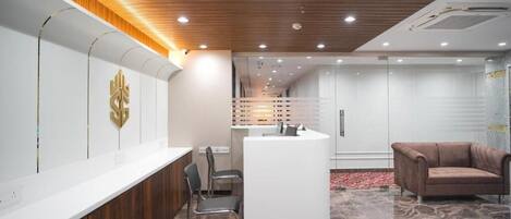 A reception area with a wooden ceiling, a reception desk, a brown leather sofa, and a patterned floor.