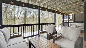 A covered outdoor seating area with wooden tables and white cushioned chairs, overlooking a forested area. - Luxury 5BR Poconos Retreat | Ski, Lake & Resort (Saw Creek)