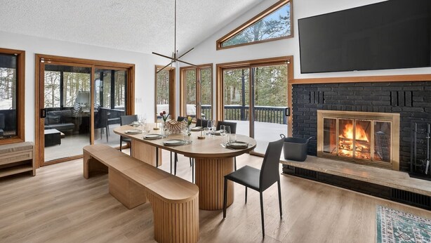 A modern dining area with a wooden table, benches, and a fireplace. - Luxury 5BR Poconos Retreat | Ski, Lake & Resort (Saw Creek)