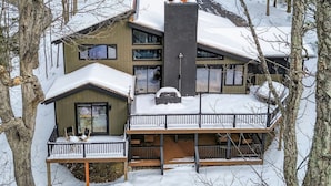 A two-story cabin with a balcony, surrounded by trees and covered in snow. - Luxury 5BR Poconos Retreat | Ski, Lake & Resort (Saw Creek)