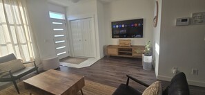 Una sala de estar con televisor, sofá, mesa de centro y una puerta que da a otra habitación.