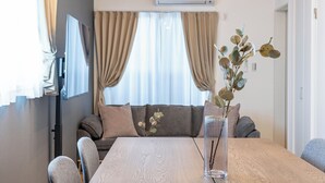 A modern living room with a sofa, a dining table, and a vase with a plant. - Farandole Sanno (Osaka)