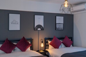 Une chambre d’hôtel avec deux lits, des oreillers rouges, un luminaire fixé au mur et des tableaux encadrés accrochés au mur.