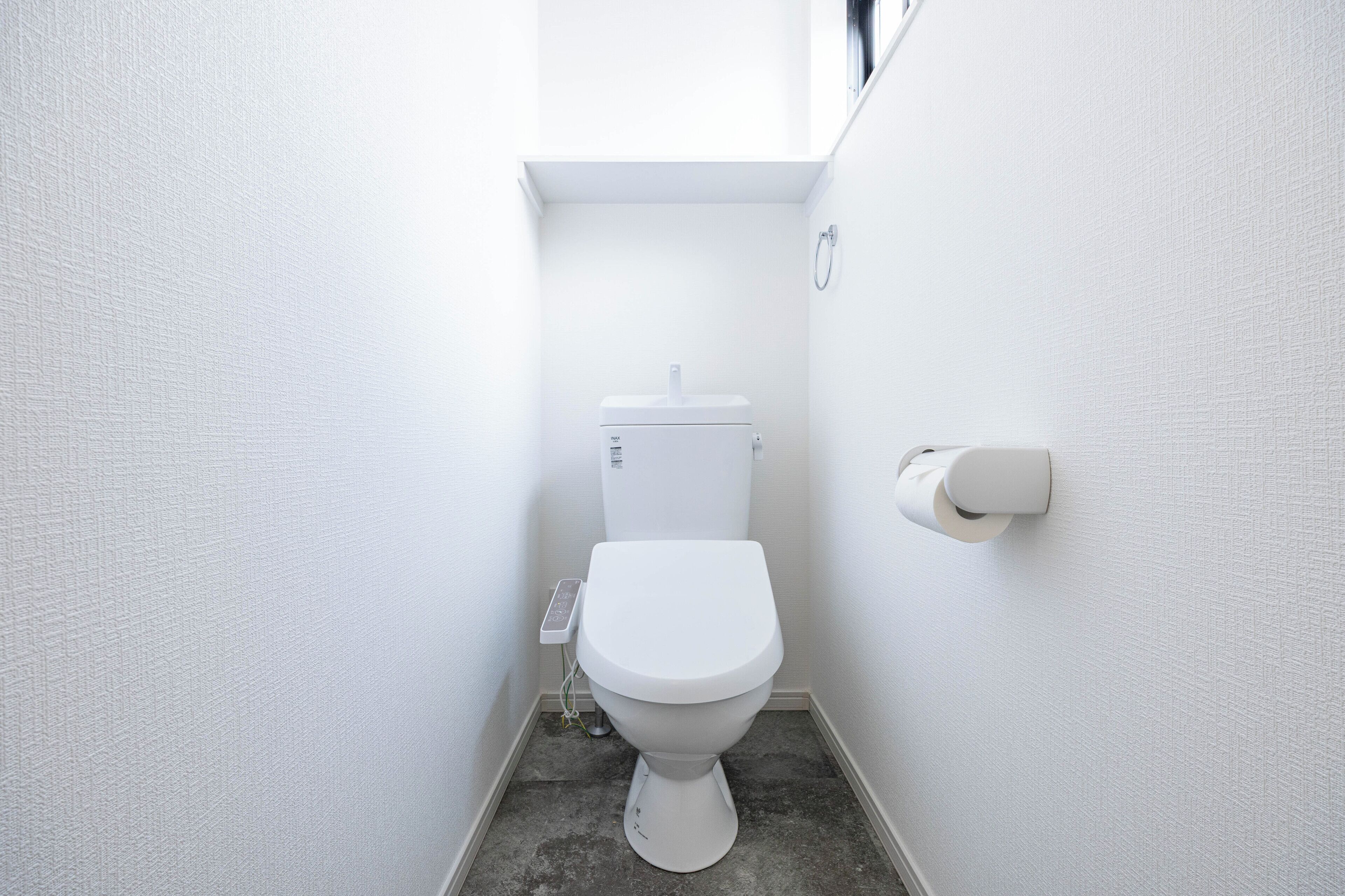 A small, white bathroom with a toilet, a toilet paper holder, and a visible electrical outlet on the wall.