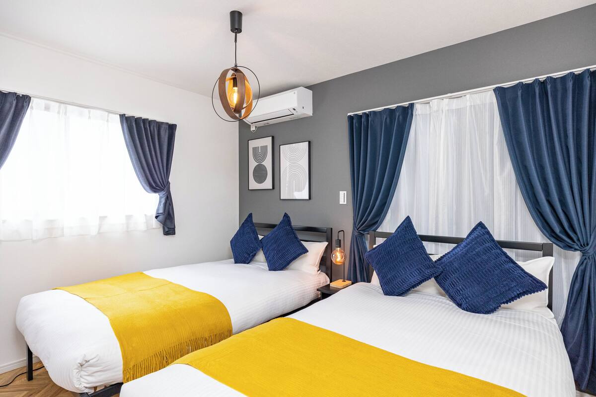 A hotel room with two beds, a ceiling light, an air conditioner, and curtains.