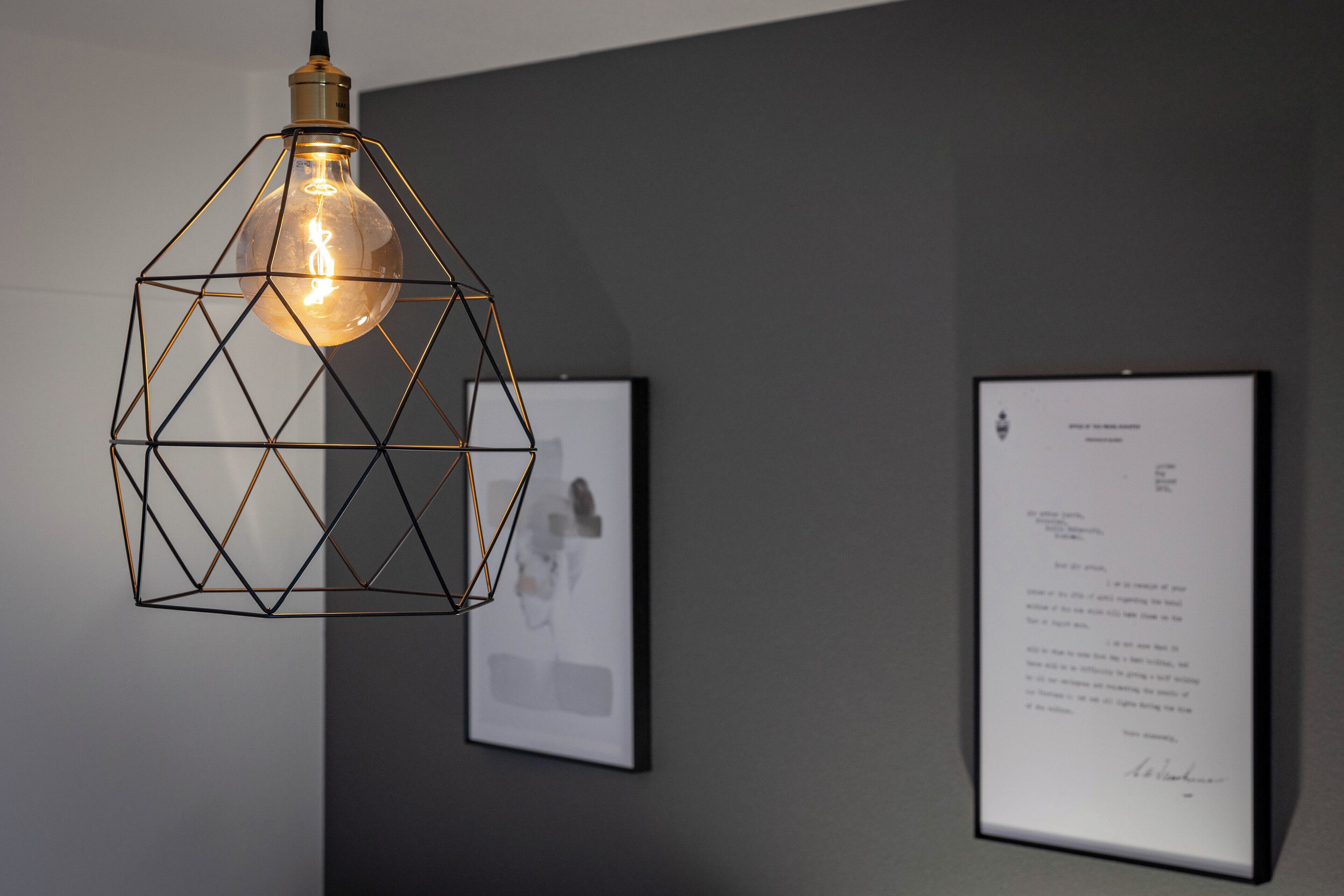 A geometric pendant light fixture with a visible filament bulb, mounted on a dark wall.