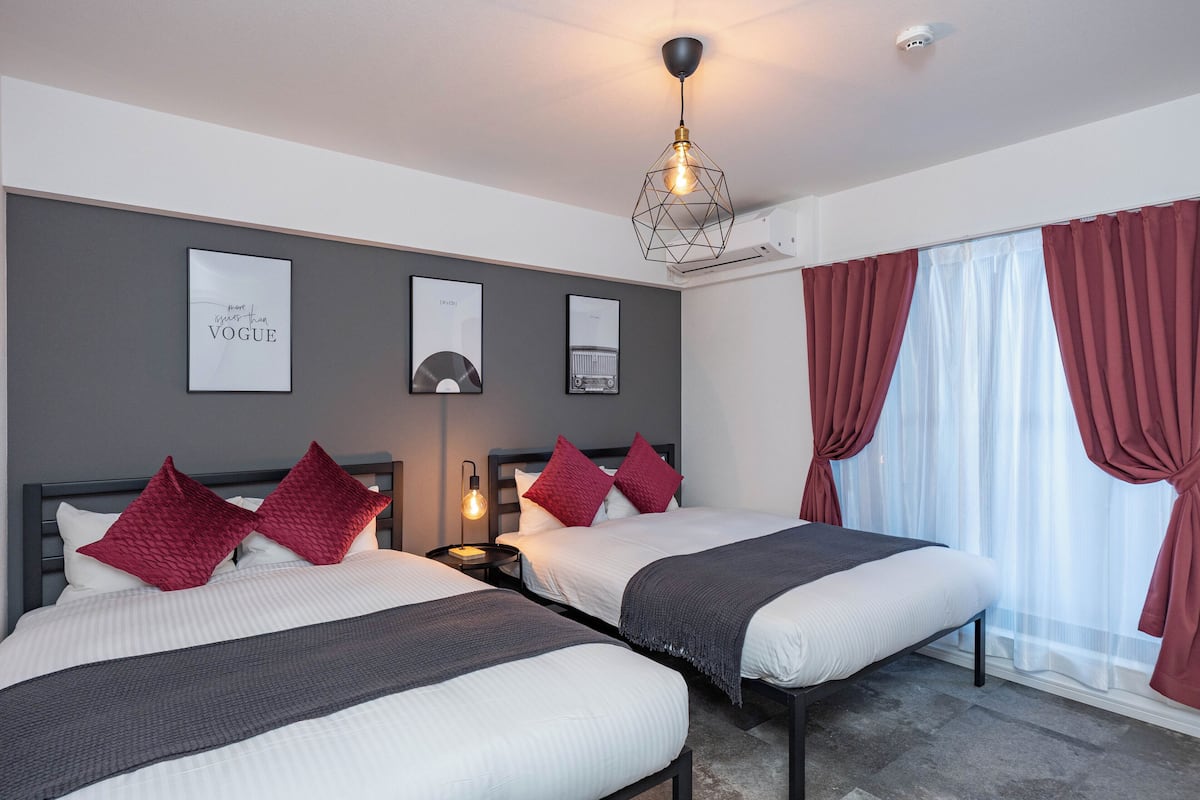 A hotel room with two beds, a nightstand, a wall-mounted light, and a window with curtains.