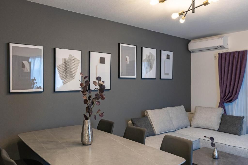 A modern living room with a grey sofa, a dining table, and framed artwork on the wall.