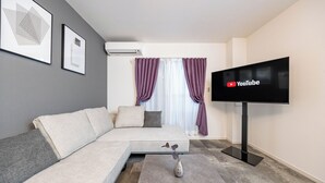 A modern living room with a sectional sofa, a flat-screen TV, and a vase on a coffee table. - Farandole Sanno (Osaka)