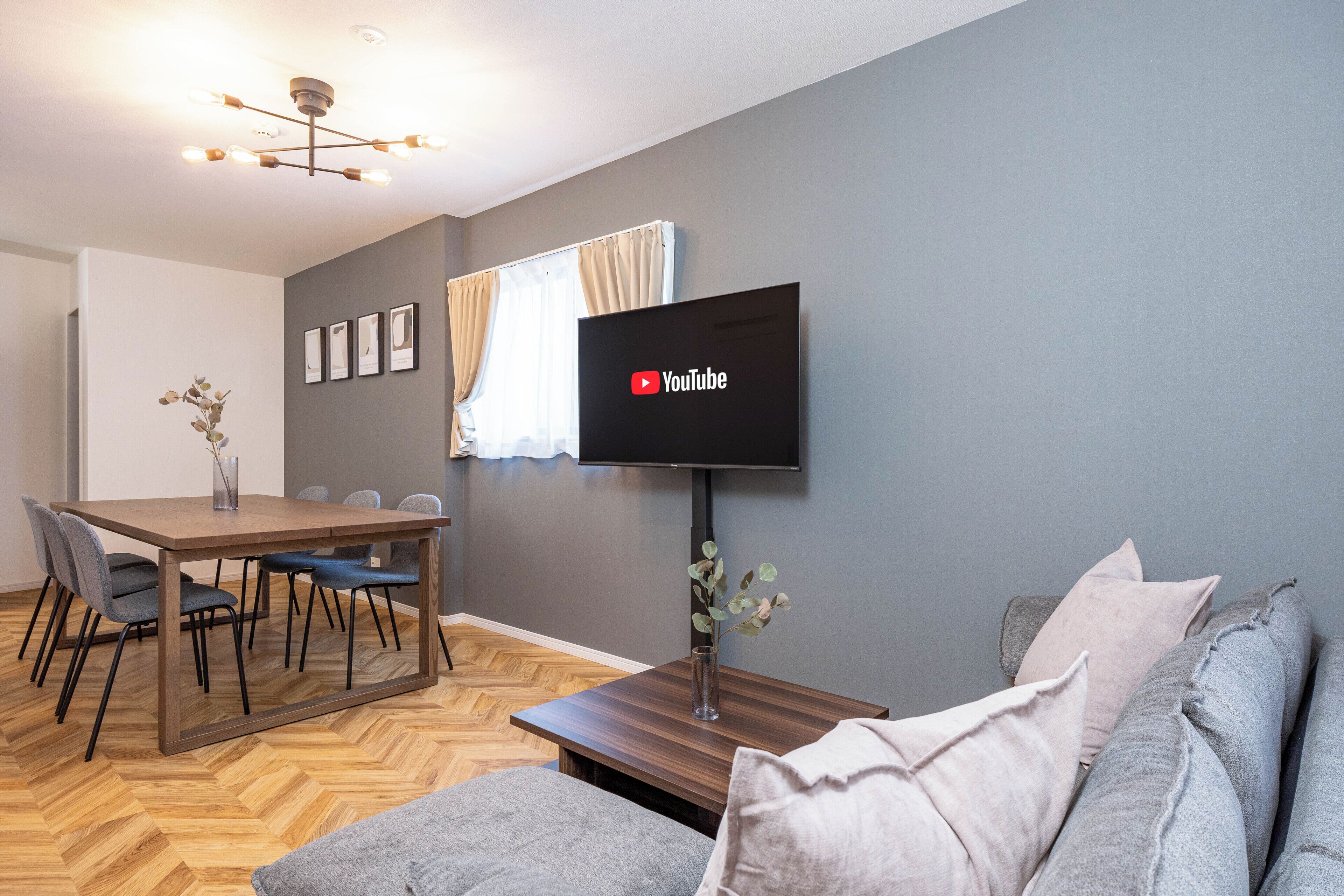A modern living room with a dining area, a flat-screen TV mounted on the wall, and a wooden coffee table.